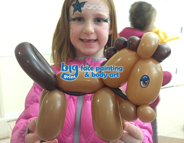 girl holding balloon twisting horse, she is face painted with flower headband